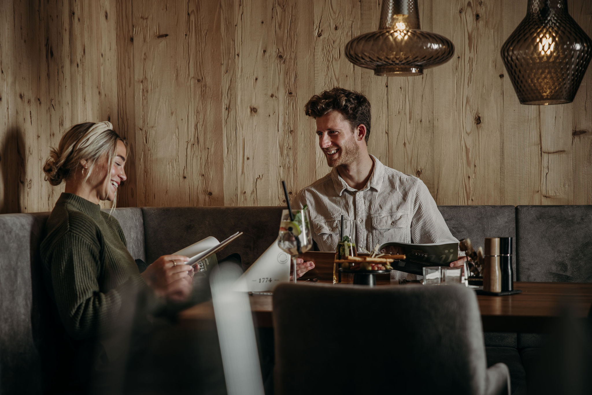 Two people smiling and reading menus at a wooden table in a cozy restaurant